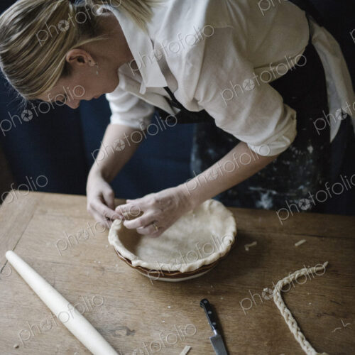 A woman working smoothing the edge of a pastry case lining a pie dish. A woman working smoothing the edge of a pastry case lining a pie dish.