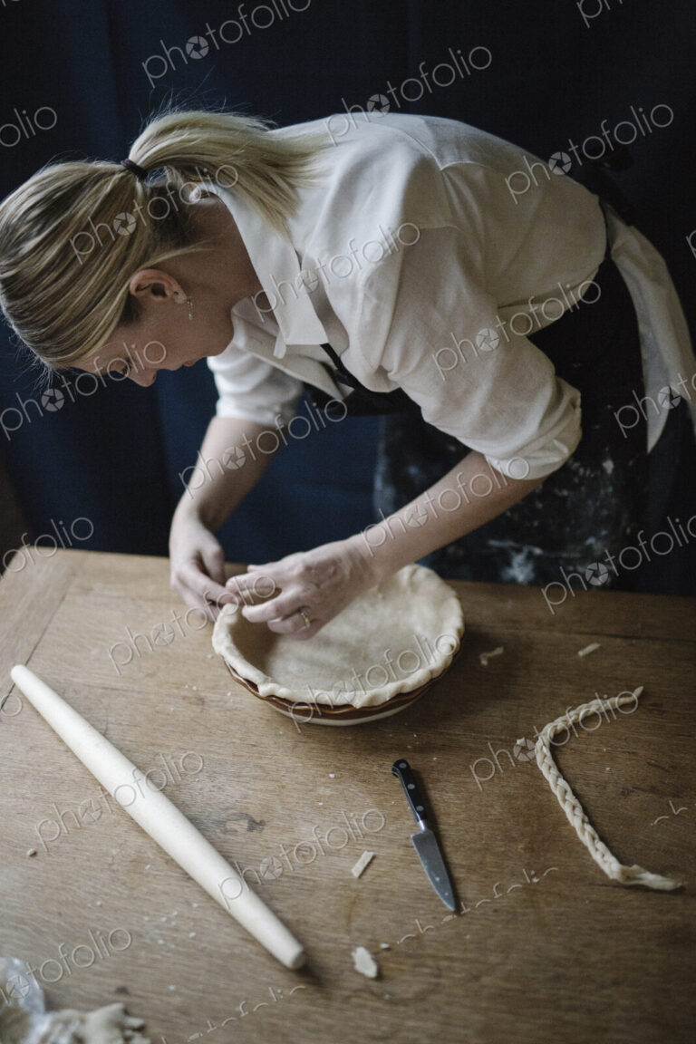 A woman working smoothing the edge of a pastry case lining a pie dish.