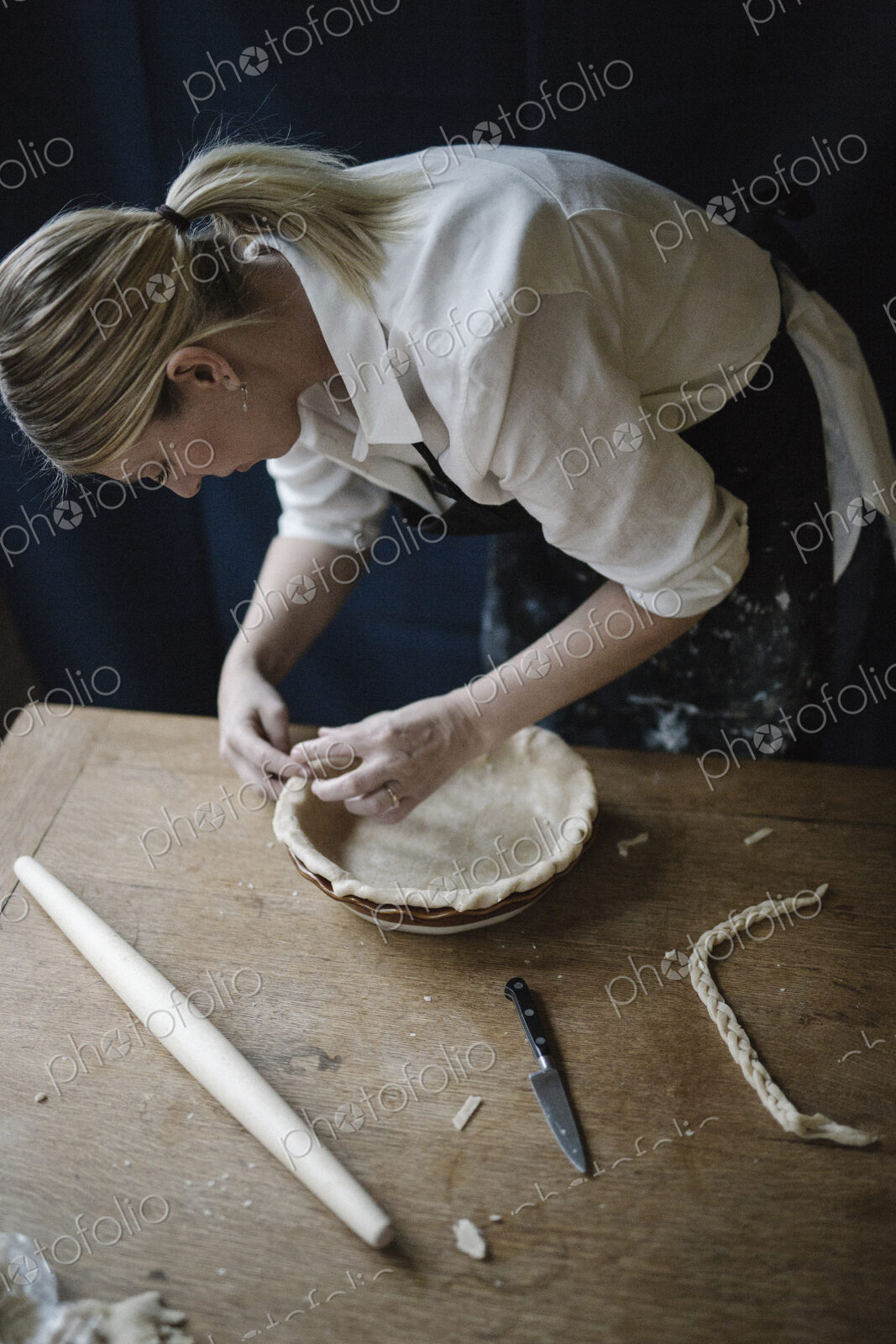 A woman working smoothing the edge of a pastry case lining a pie dish.