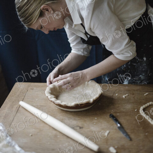 A woman working smoothing the edge of a pastry case lining a pie dish. A woman working smoothing the edge of a pastry case lining a pie dish.