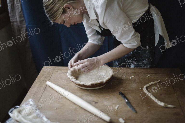 A woman working smoothing the edge of a pastry case lining a pie dish.