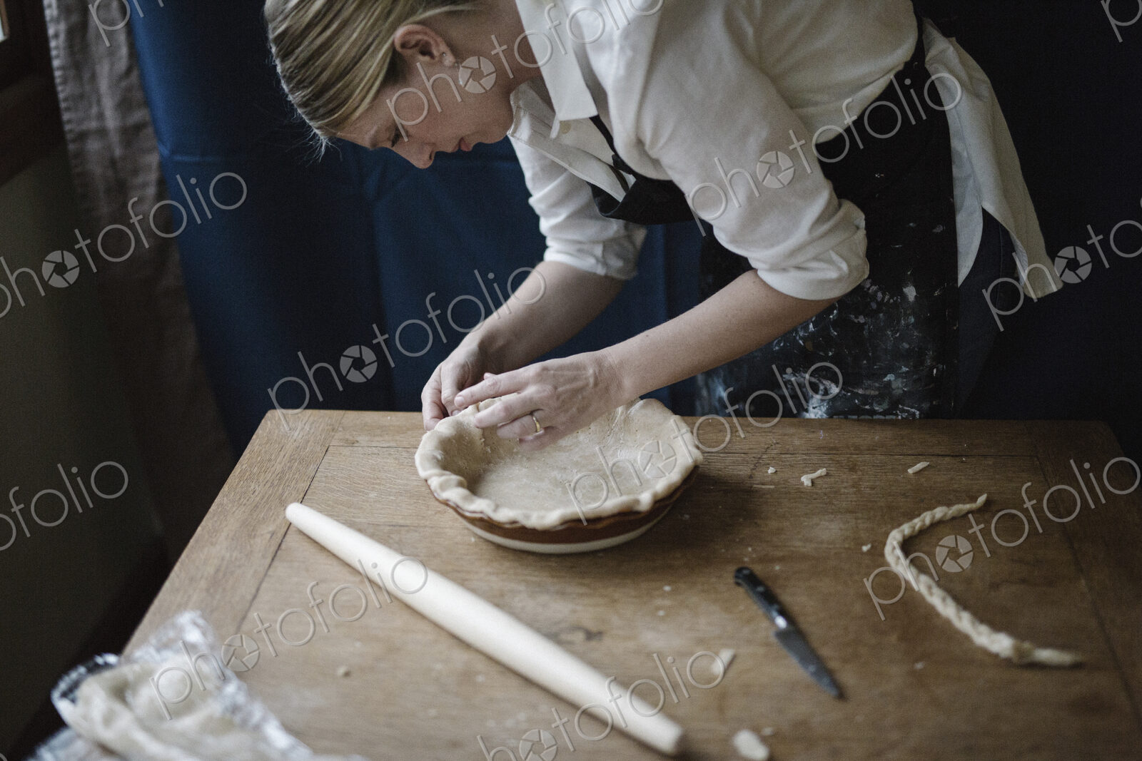 A woman working smoothing the edge of a pastry case lining a pie dish.