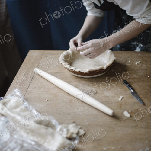 A woman working smoothing the edge of a pastry case lining a pie dish. A woman working smoothing the edge of a pastry case lining a pie dish.