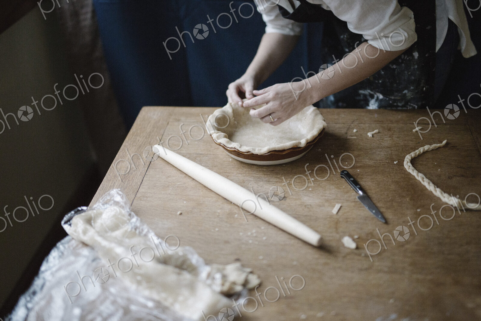 A woman working smoothing the edge of a pastry case lining a pie dish.