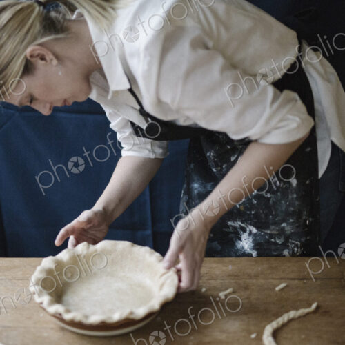A woman working smoothing the edge of a pastry case lining a pie dish. A woman working smoothing the edge of a pastry case lining a pie dish.