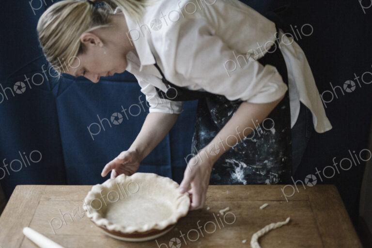 A woman working smoothing the edge of a pastry case lining a pie dish.