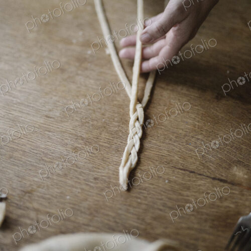 A woman working with raw pastry, plaiting three strands of dough.