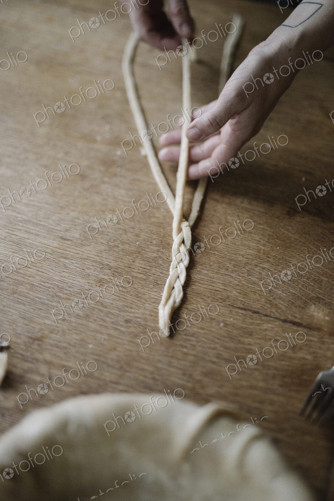 A woman working with raw pastry, plaiting three strands of dough.