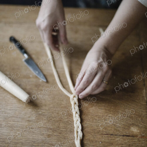 A woman working with raw pastry, plaiting three strands of dough.
