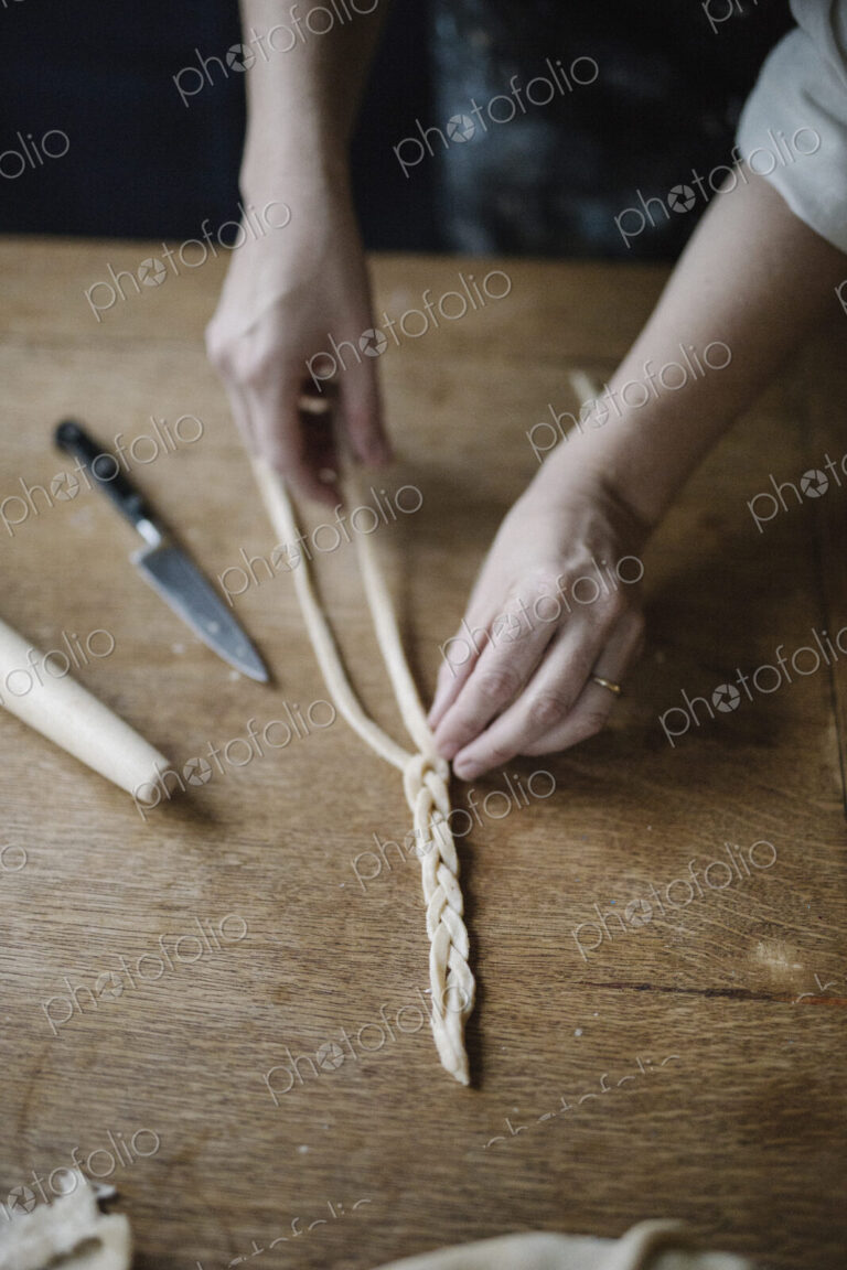 A woman working with raw pastry, plaiting three strands of dough.