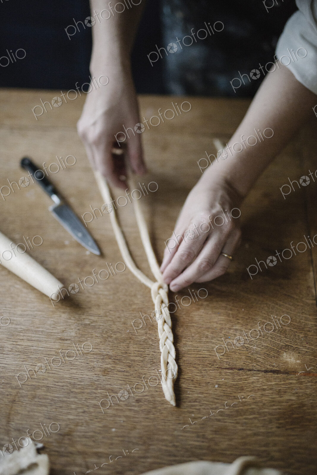 A woman working with raw pastry, plaiting three strands of dough.