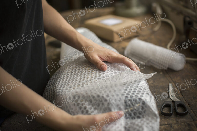 A woman wrapping an item in bubble wrap, a parcel being prepared for despatch.