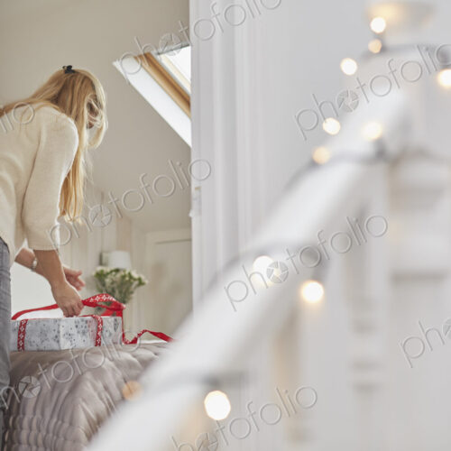 A woman wrapping red ribbons around Christmas presents on a bed, view through the… A woman wrapping red ribbons around Christmas presents on a bed, view through the…