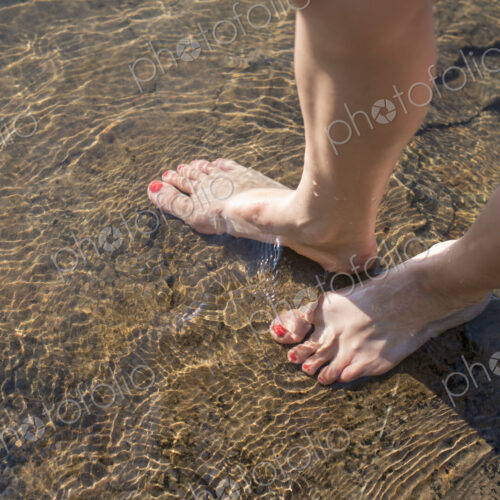 A woman's bare feet in the sand by the lake shore.