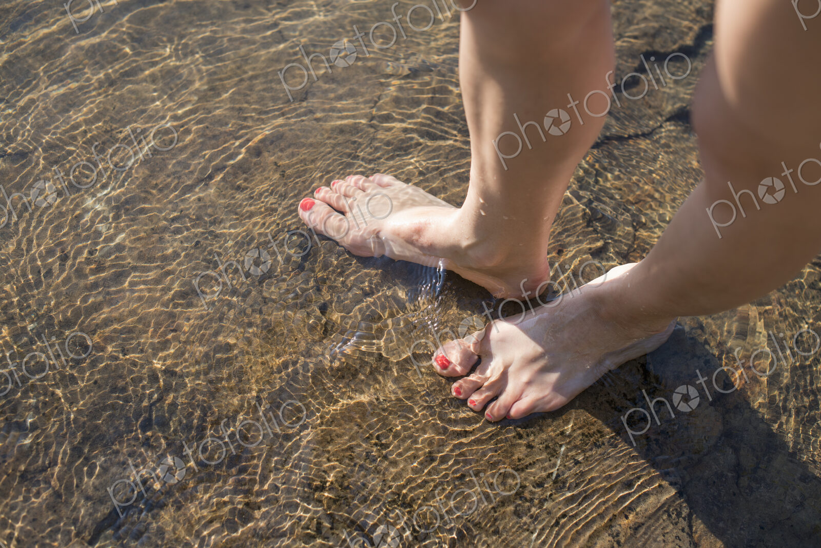 A woman’s bare feet in the sand by the lake shore.