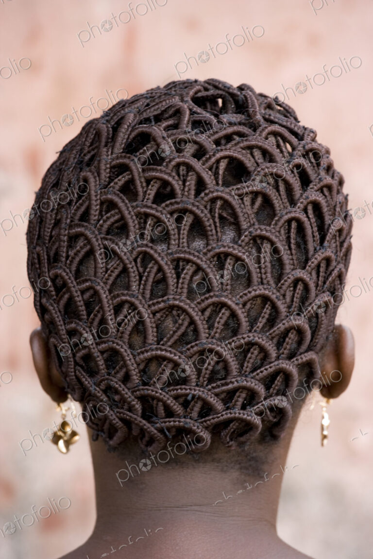 A woman's head with braided patterned hair and earrings.