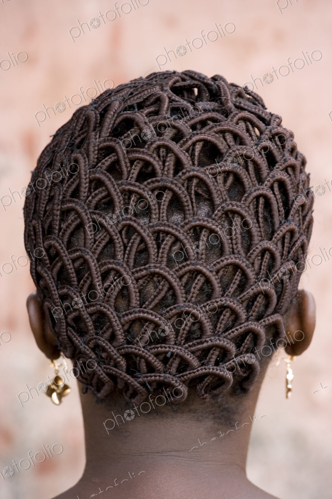 A woman’s head with braided patterned hair and earrings.