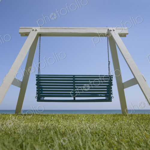 A wooden beach swing with a green painted seat and view of the sea.