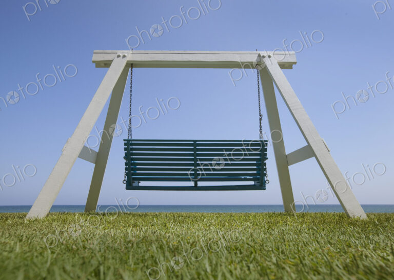 A wooden beach swing with a green painted seat and view of the sea.