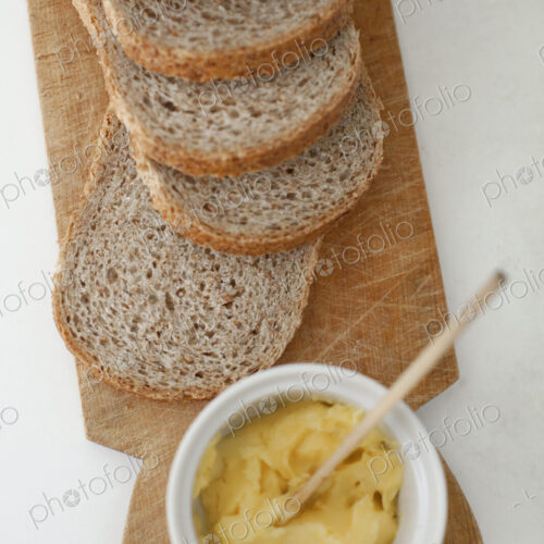 A wooden breadboard with a sliced brown loaf laid out. A dish of butter with a wooden… A wooden breadboard with a sliced brown loaf laid out. A dish of butter with a wooden…
