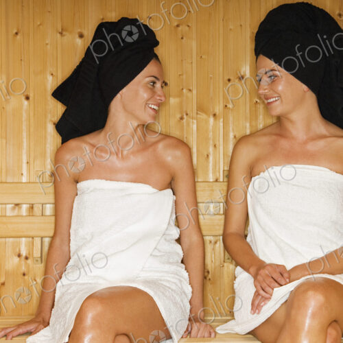 A wooden panneled sauna. Two women seated talking. A wooden panneled sauna. Two women seated talking.
