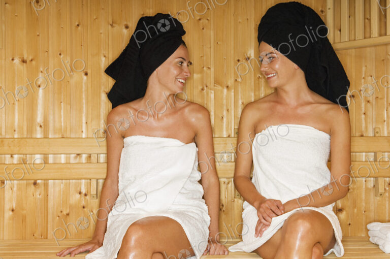 A wooden panneled sauna. Two women seated talking.