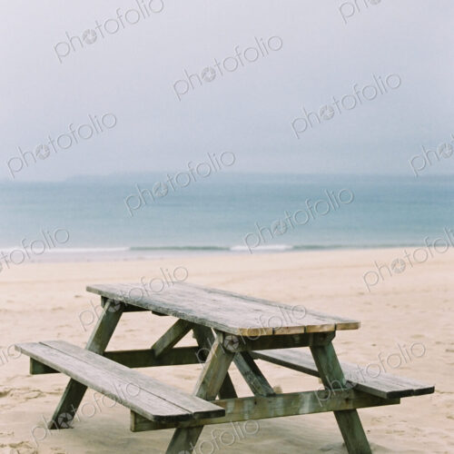 A wooden picnic bench on the sand. View out to sea. A wooden picnic bench on the sand. View out to sea.
