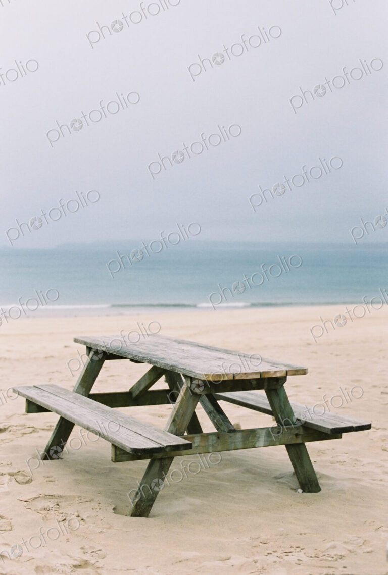 A wooden picnic bench on the sand. View out to sea.
