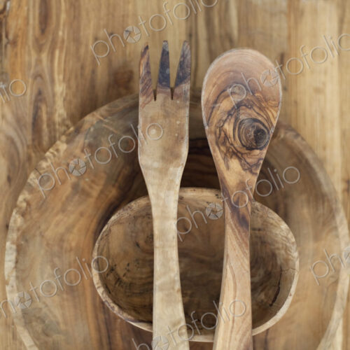 A wooden table top with two small turned bowls and two wooden salad servers. Wood…