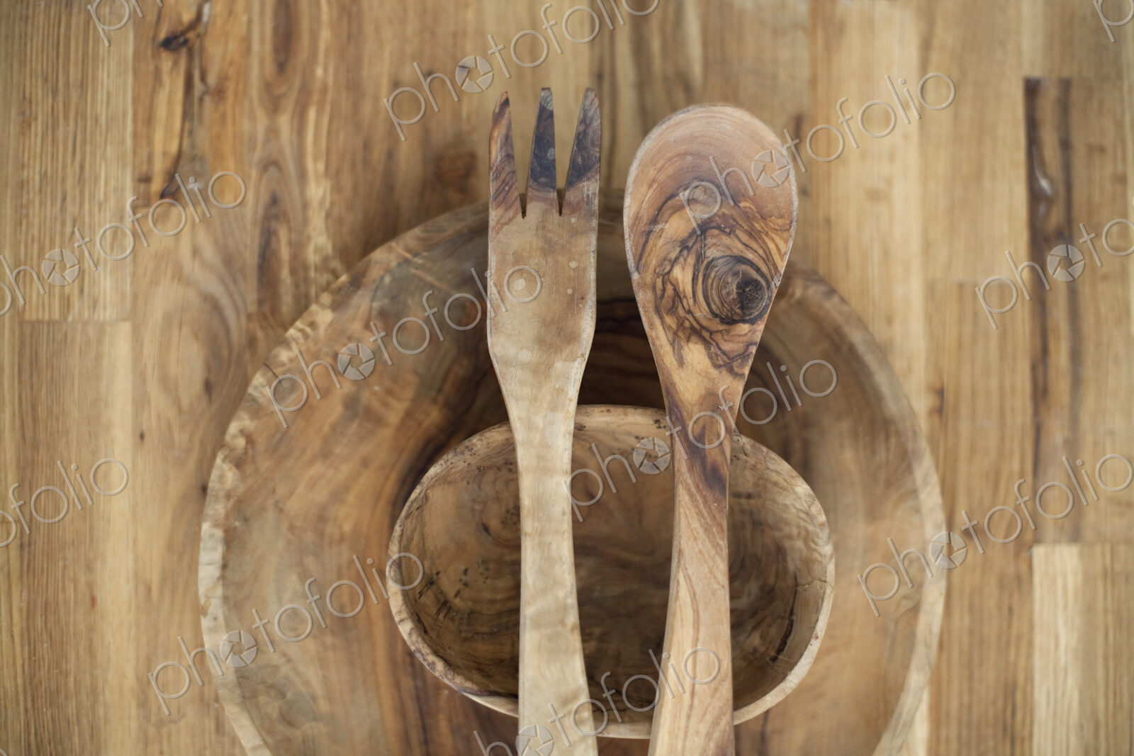 A wooden table top with two small turned bowls and two wooden salad servers. Wood…