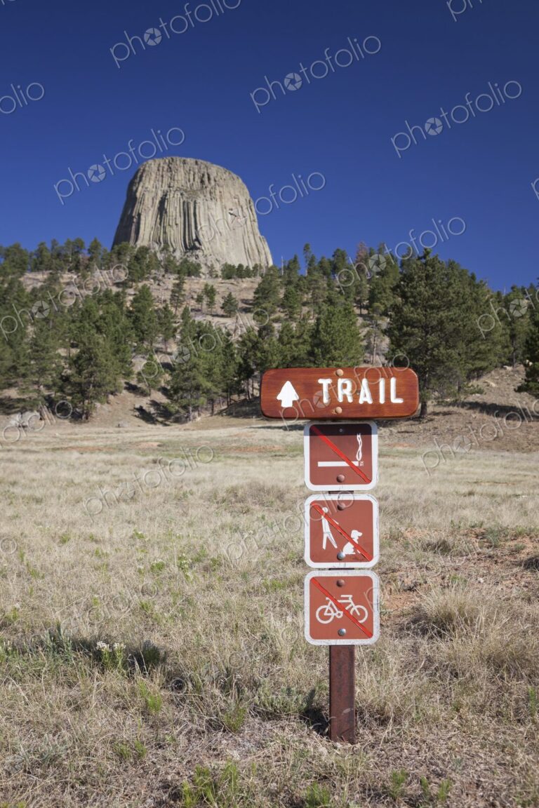 A wooden trail sign with hiking regulations stands in front of Devil's Tower National…
