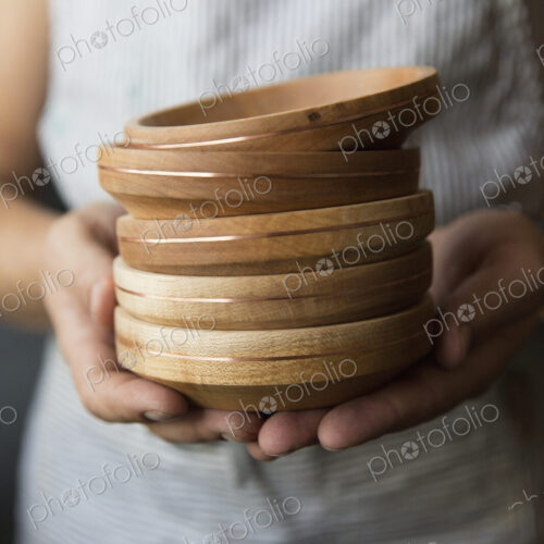 A woodworker holding a stack of turned wood bowls or dishes.