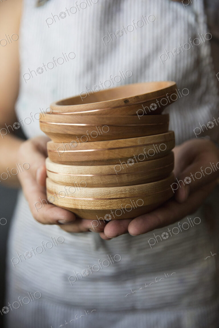 A woodworker holding a stack of turned wood bowls or dishes.