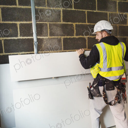 A workman in hard hat and high vis jacket stacking wood against a wall at a… A workman in hard hat and high vis jacket stacking wood against a wall at a…