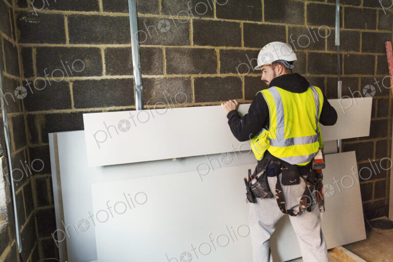 A workman in hard hat and high vis jacket stacking wood against a wall at a…