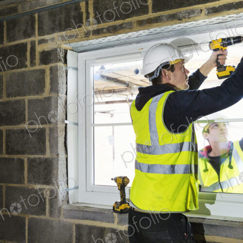 A workman on a construction site, a builder in hard hat using an electric drill on a…