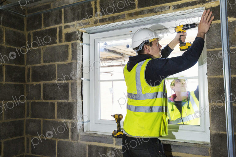 A workman on a construction site, a builder in hard hat using an electric drill on a…