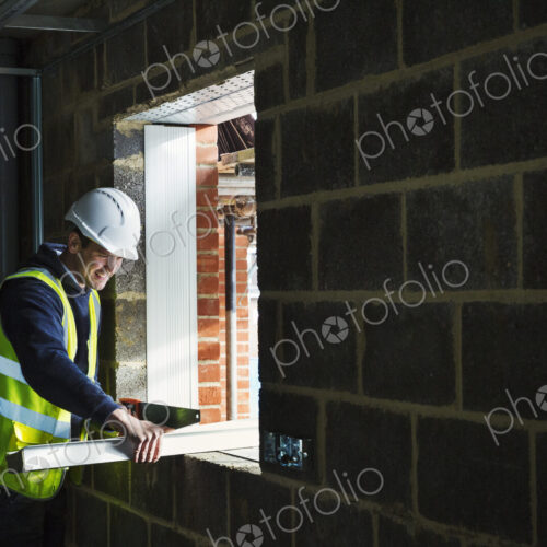 A workman on a construction site, builder in hard hat using a saw on a piece of wood.