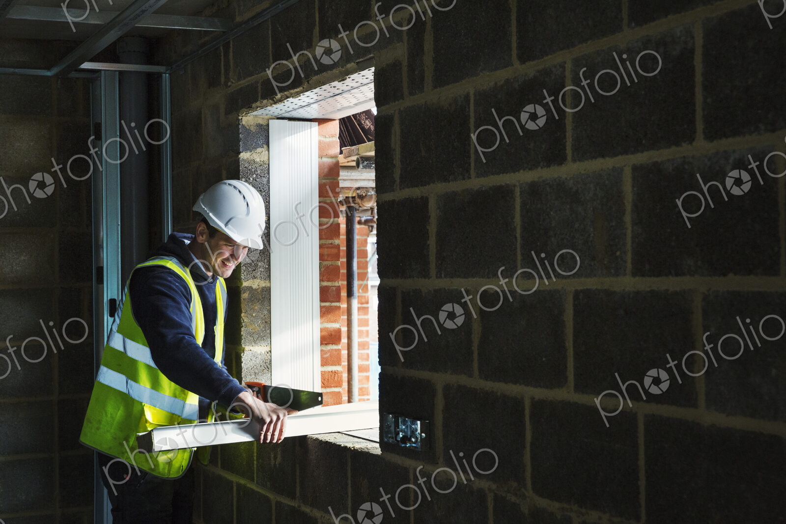 A workman on a construction site, builder in hard hat using a saw on a piece of wood.