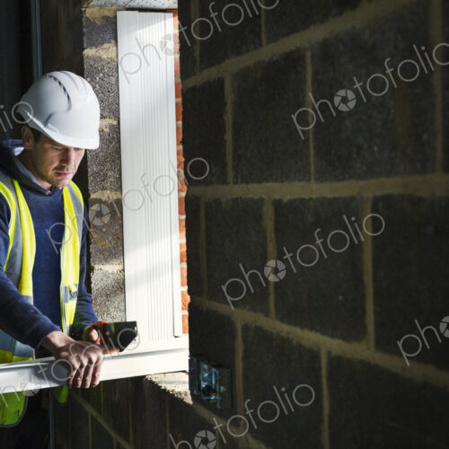 A workman on a construction site, builder in hard hat using a saw on a plank of wood.