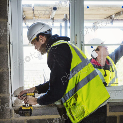 A workman on a construction site, builder in hard hat using an electric drill on a…