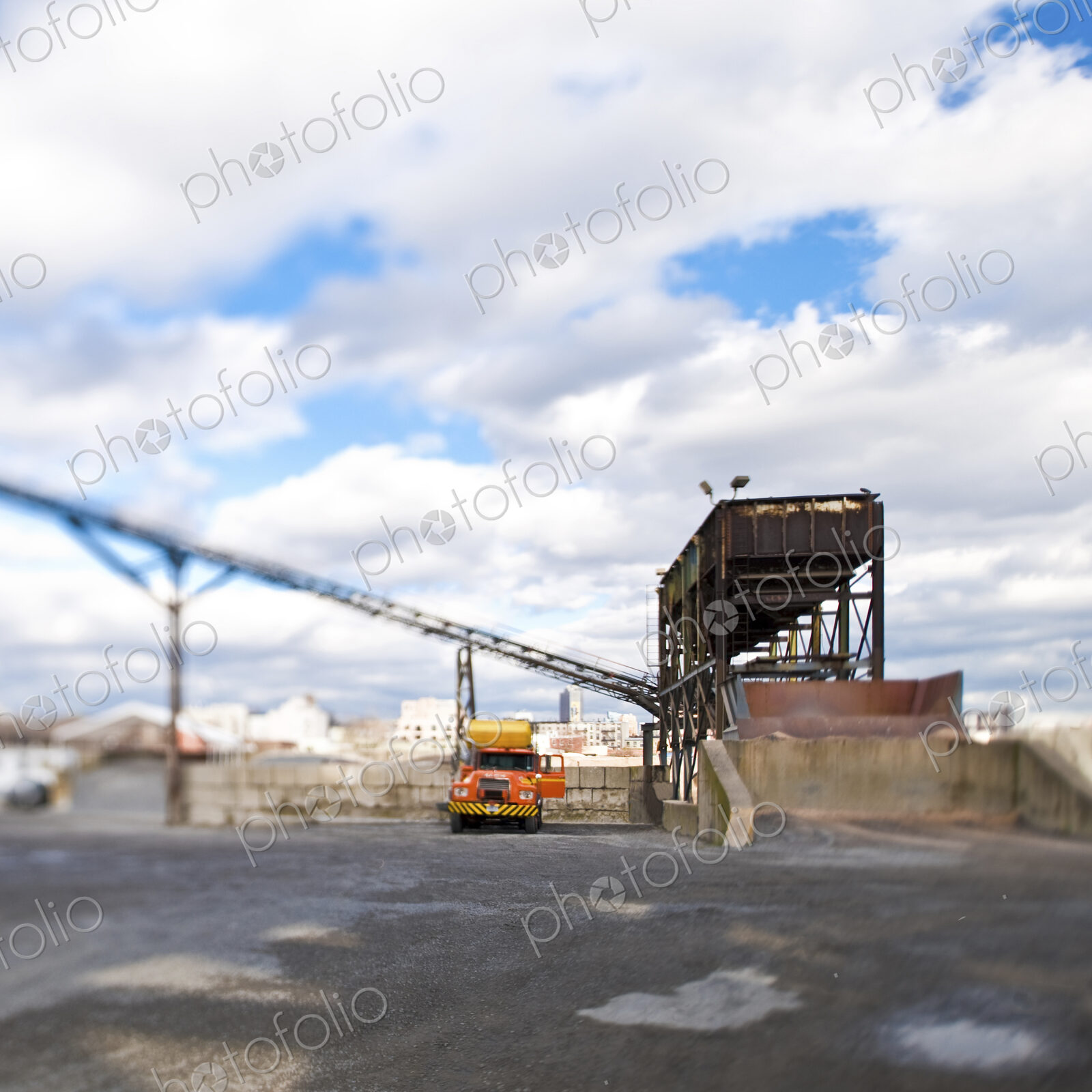 A yellow truck parked at a loading bay, elevated weighbridge and overhead bridge.