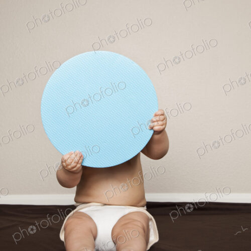A young 8 month old baby boy wearing cloth diapers, hiding behind a large blue disc. A young 8 month old baby boy wearing cloth diapers, hiding behind a large blue disc.