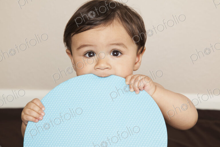 A young 8 month old baby boy wearing cloth diapers, holding a large blue disc and…