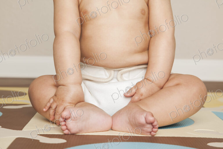 A young 8 month old baby boy wearing cloth diapers, sitting on the floor.