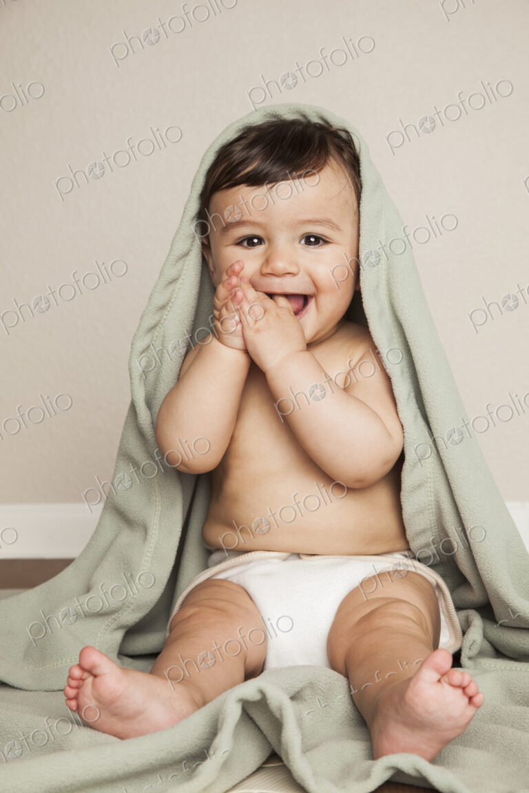 A young 8 month old baby boy wearing cloth diapers, sitting on the floor. A cot…