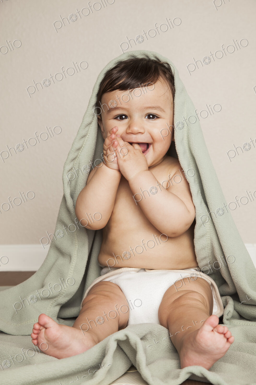 A young 8 month old baby boy wearing cloth diapers, sitting on the floor. A cot…