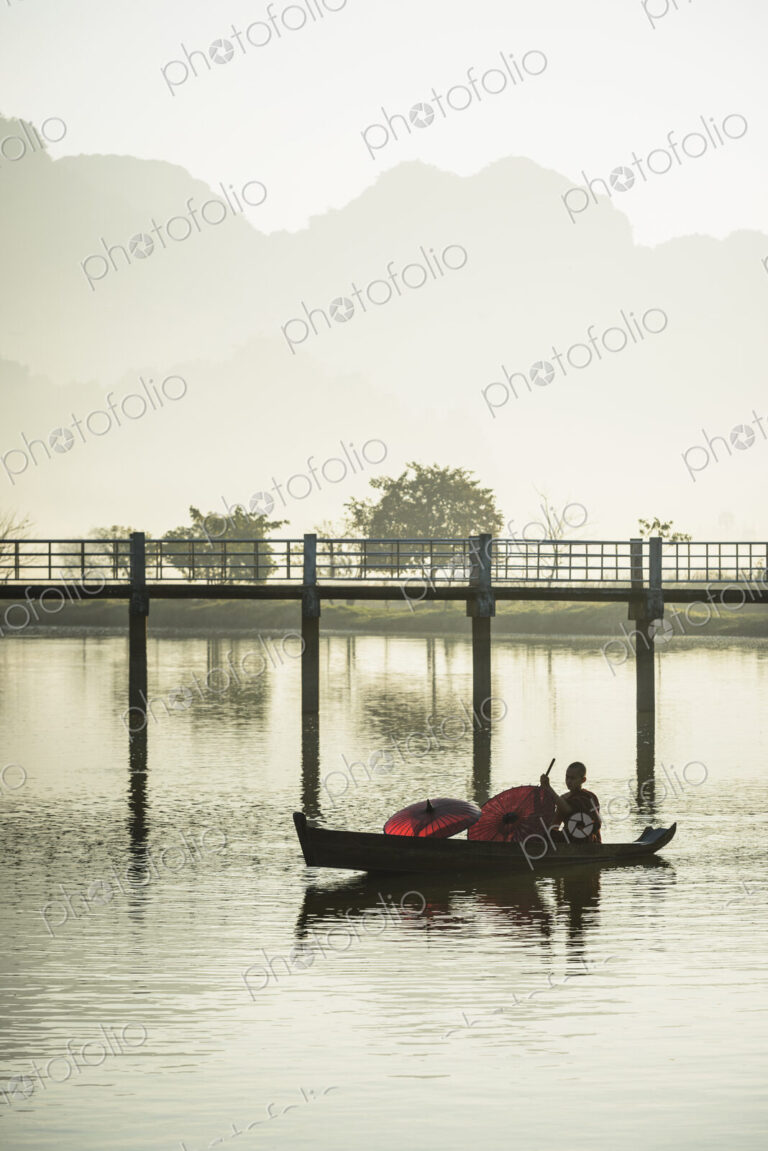 A young Buddist monk paddling a wooden boat along a river.