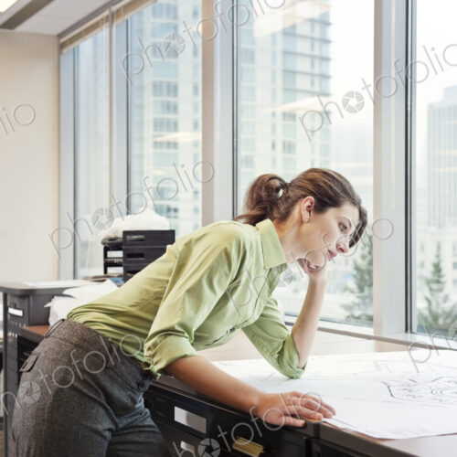 A young Caucasian businesswoman looking over plans for a new space in her in office. A young Caucasian businesswoman looking over plans for a new space in her in office.