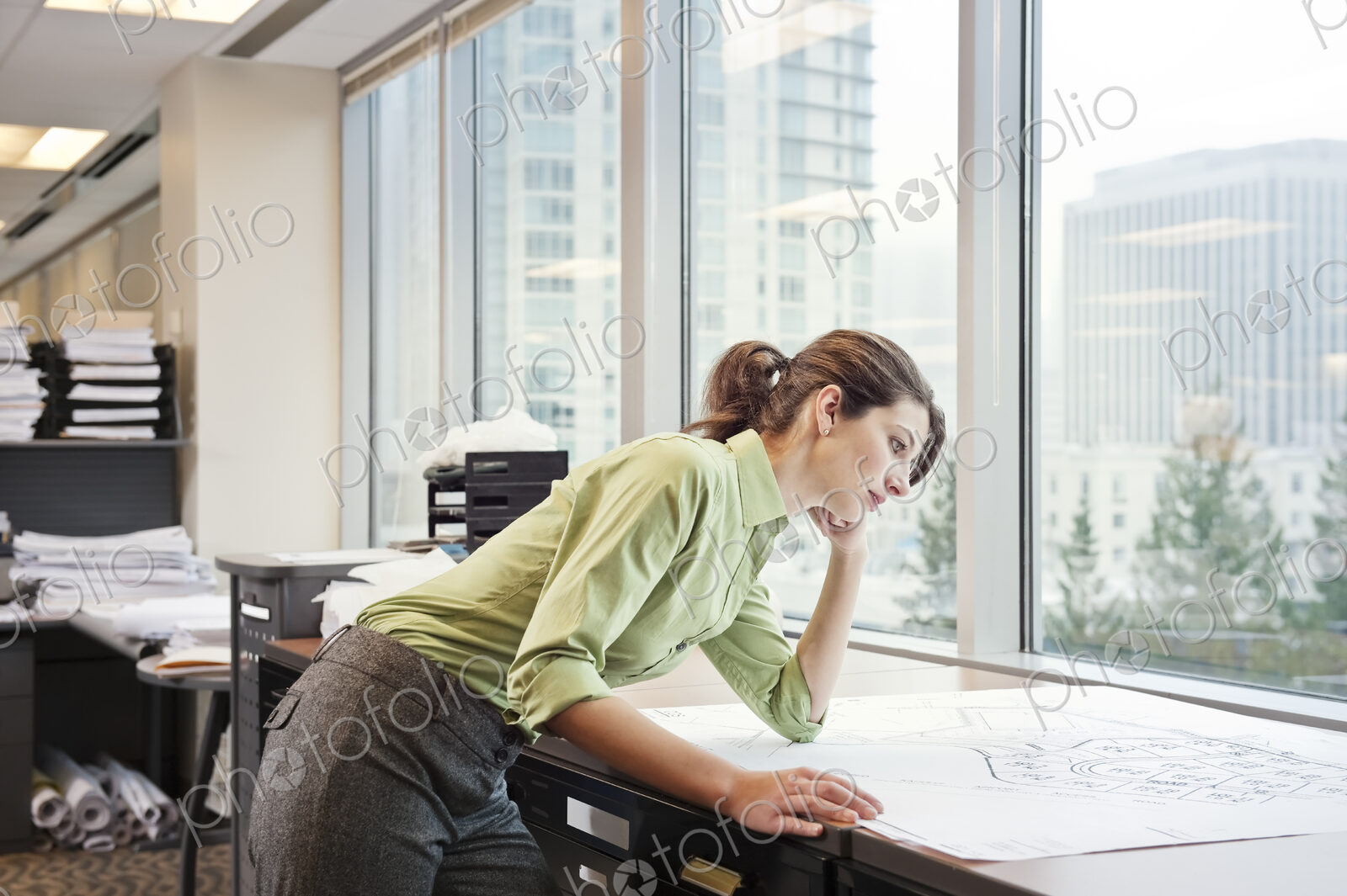 A young Caucasian businesswoman looking over plans for a new space in her in office.